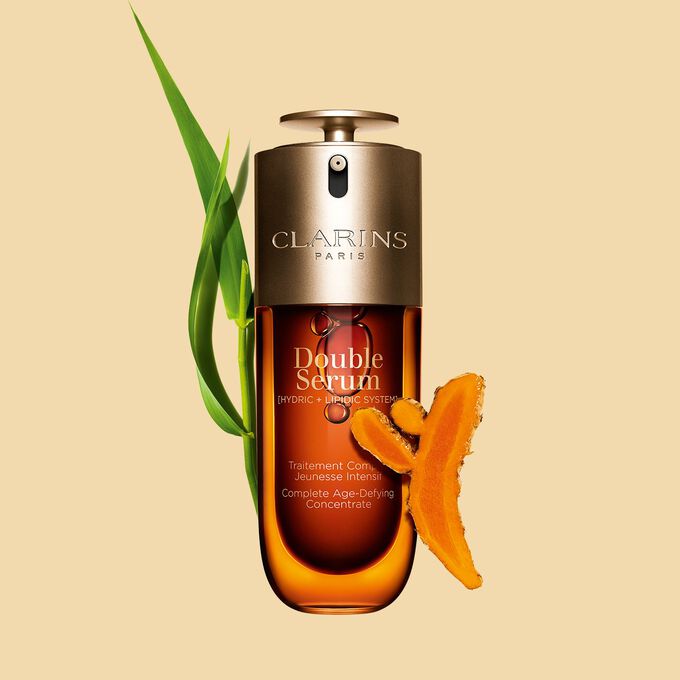 Abbildung von Clarins Double Serum vor den Hauptinhaltsstoffen Curcuma und Pfahlrohr auf einem goldenen Hintergrund